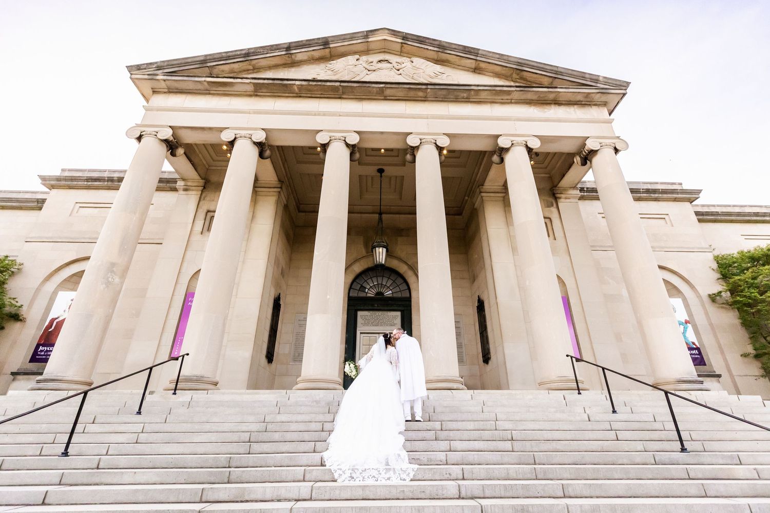Wedding couple standing on grand steps of a neoclassical building with columned entrance.