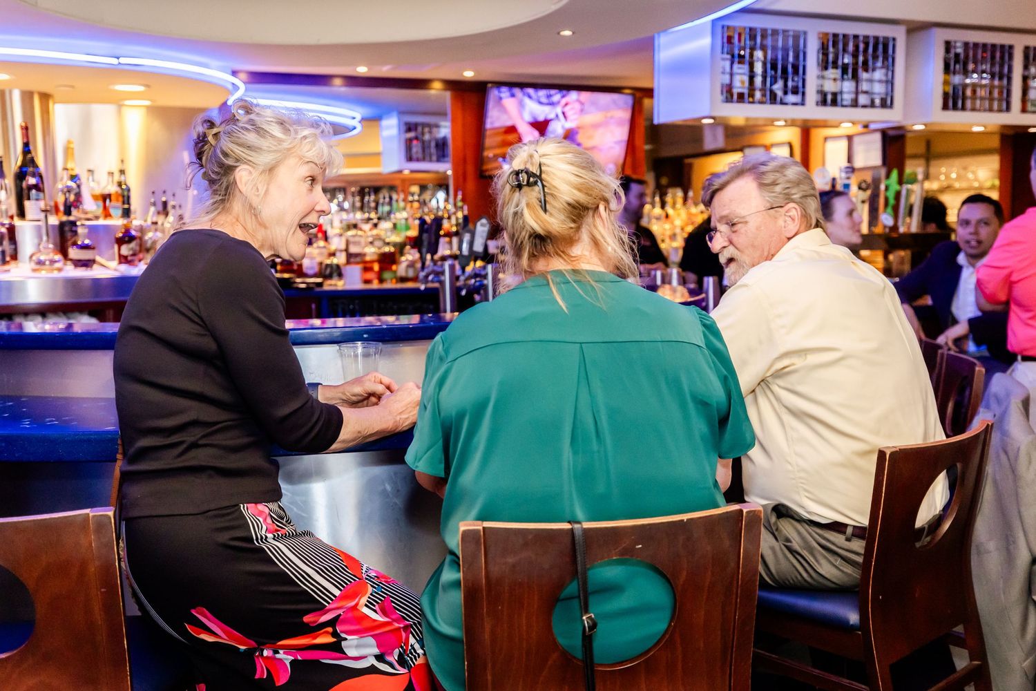 Three people engaged in conversation while seated at a bar counter.