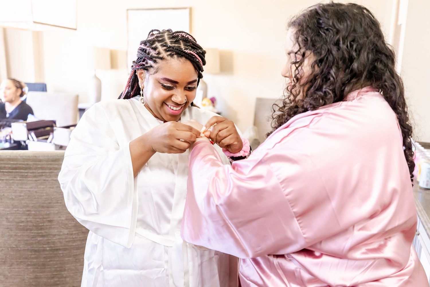 Two people sharing a joyful moment while getting ready in white and pink robes.