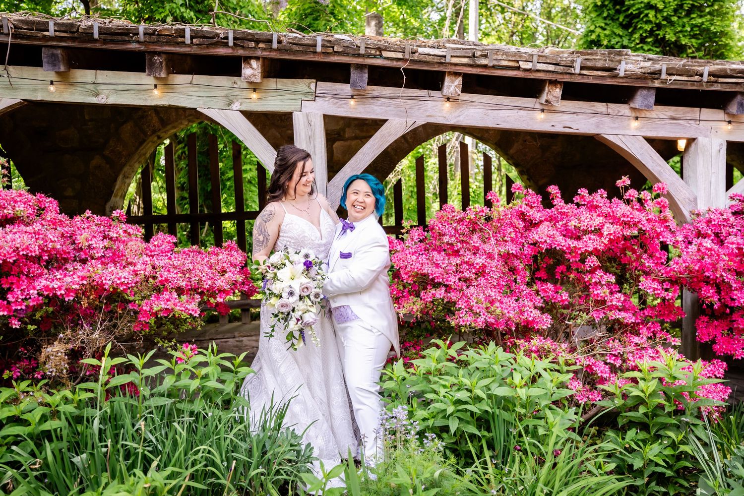 A couple celebrates their wedding day surrounded by blooming pink azaleas and greenery.