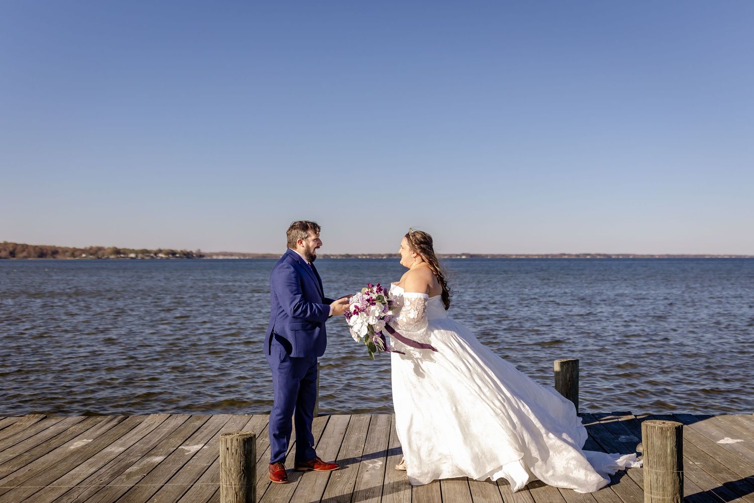 Wedding couple standing on waterfront dock during sunset with ocean view in background.