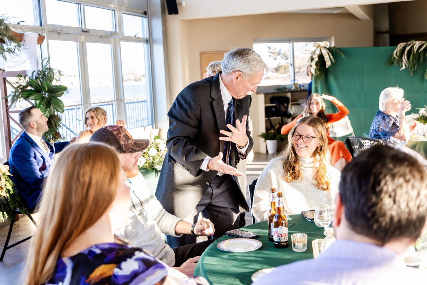 Wedding reception scene with guests seated at tables while someone speaks standing.