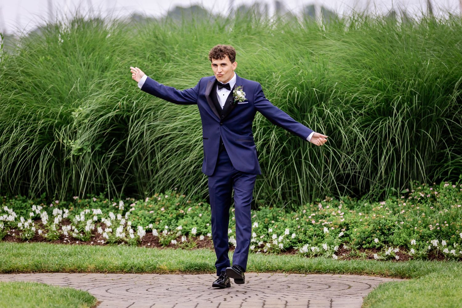 Person in a navy suit strikes playful poses on a stone pathway surrounded by greenery.