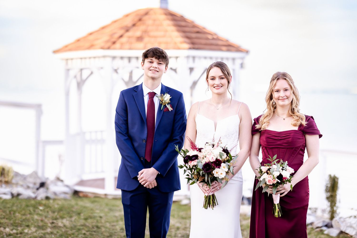 Wedding party poses outdoors with bridesmaids in burgundy dresses.