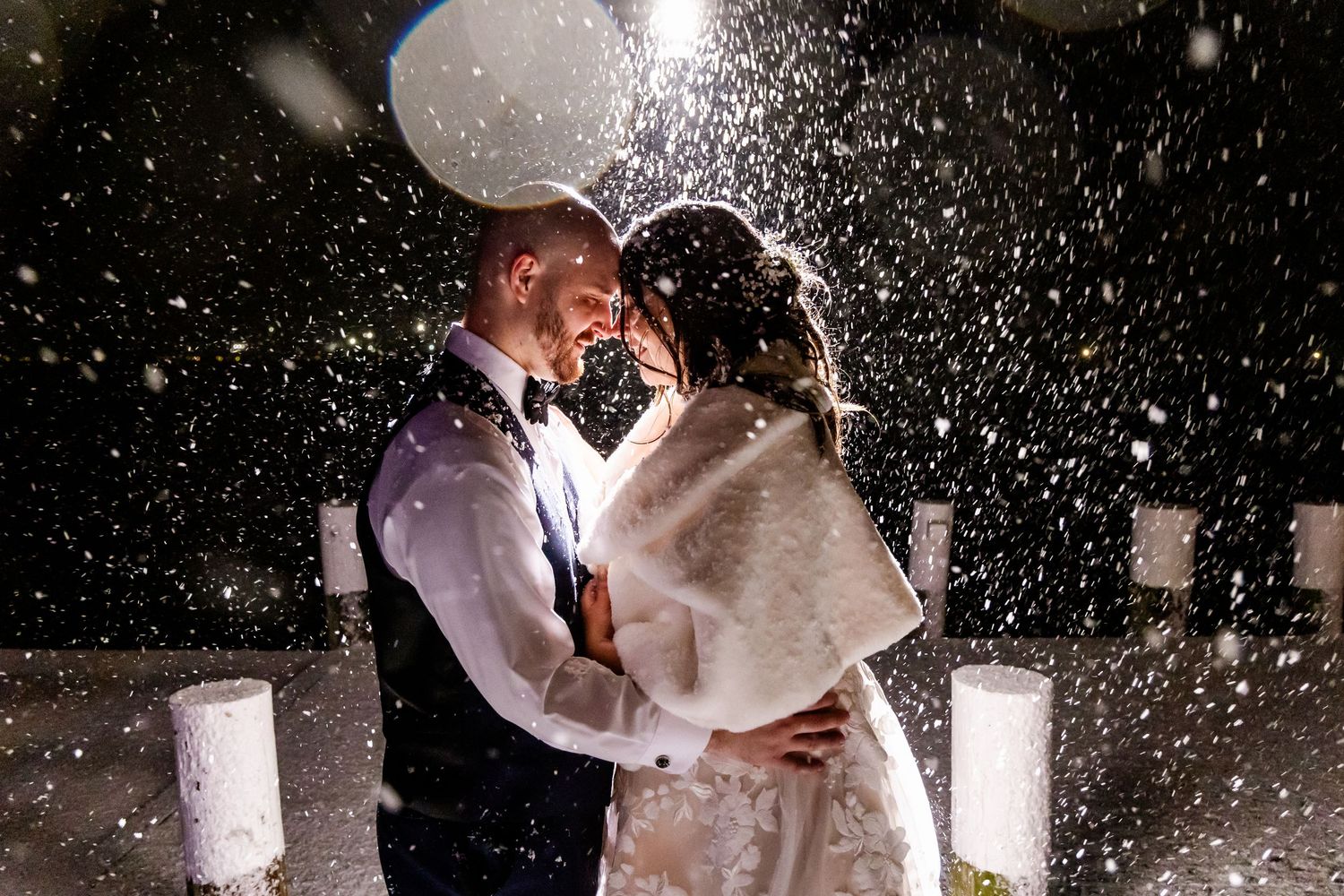A romantic couple shares a magical kiss in the snow surrounded by glowing lanterns at night during their winter wedding celebration.