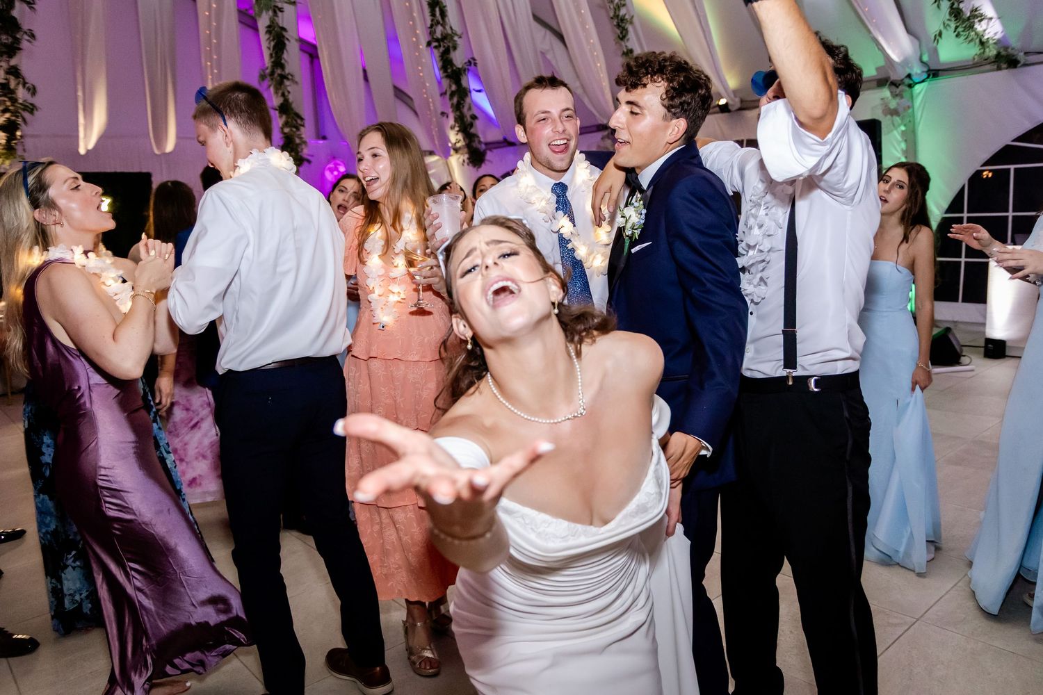 Guests dancing and celebrating at an elegant wedding reception with purple ambient lighting.