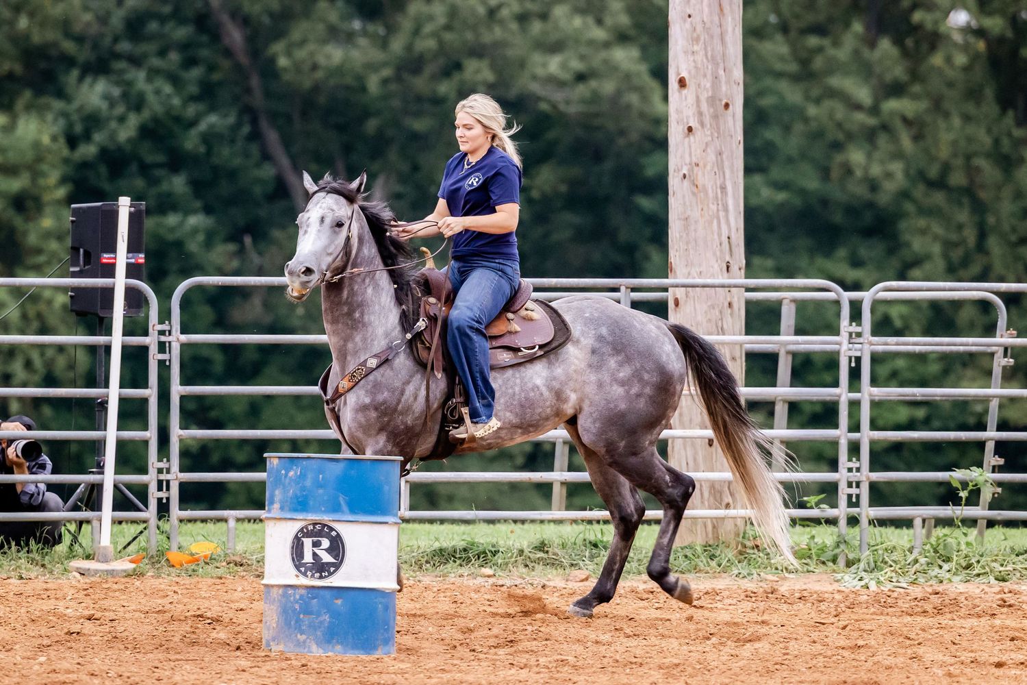 Horse and rider compete in barrel racing, making tight turns around barrels in an outdoor arena.