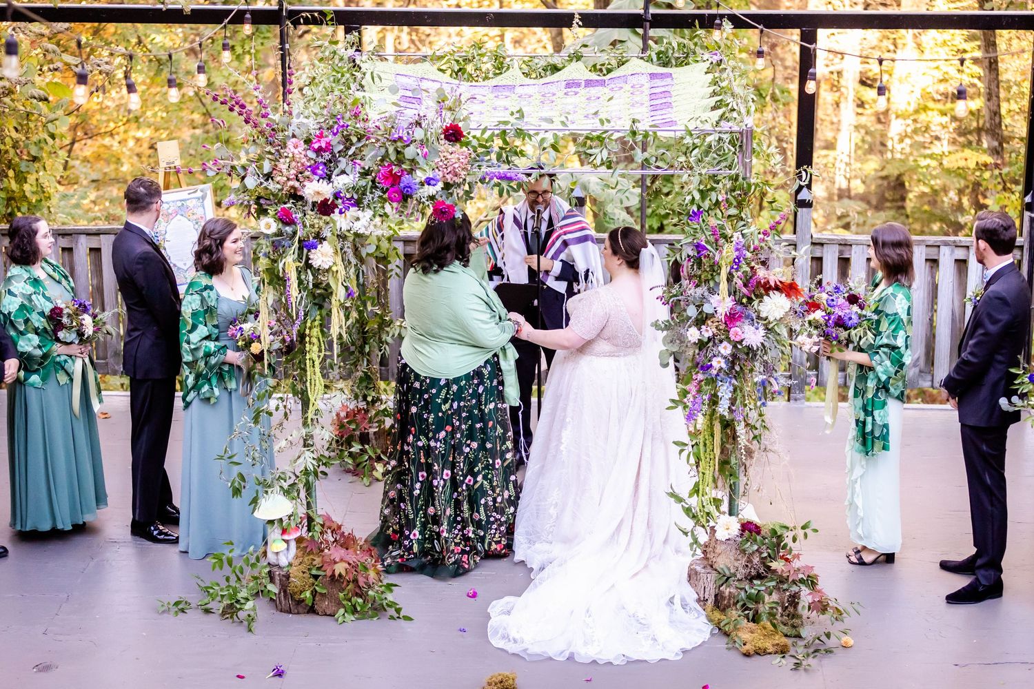 Beautiful floral wedding ceremony setup with purple flowers and greenery under outdoor pavilion.