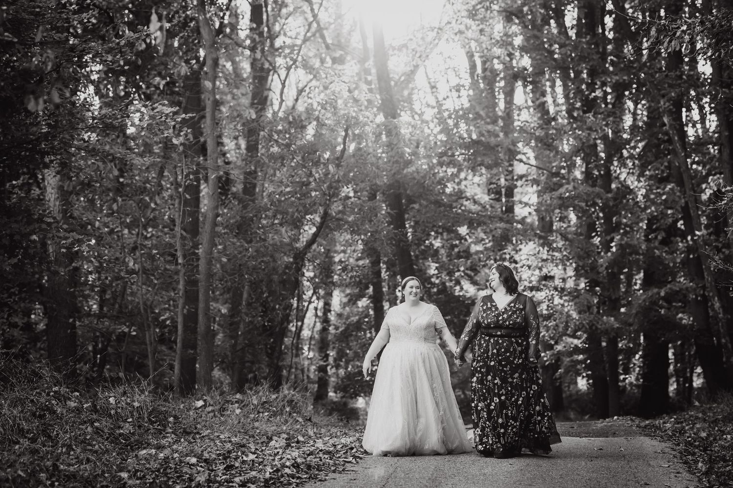 Black and white photo of two people walking together in a wooded path.