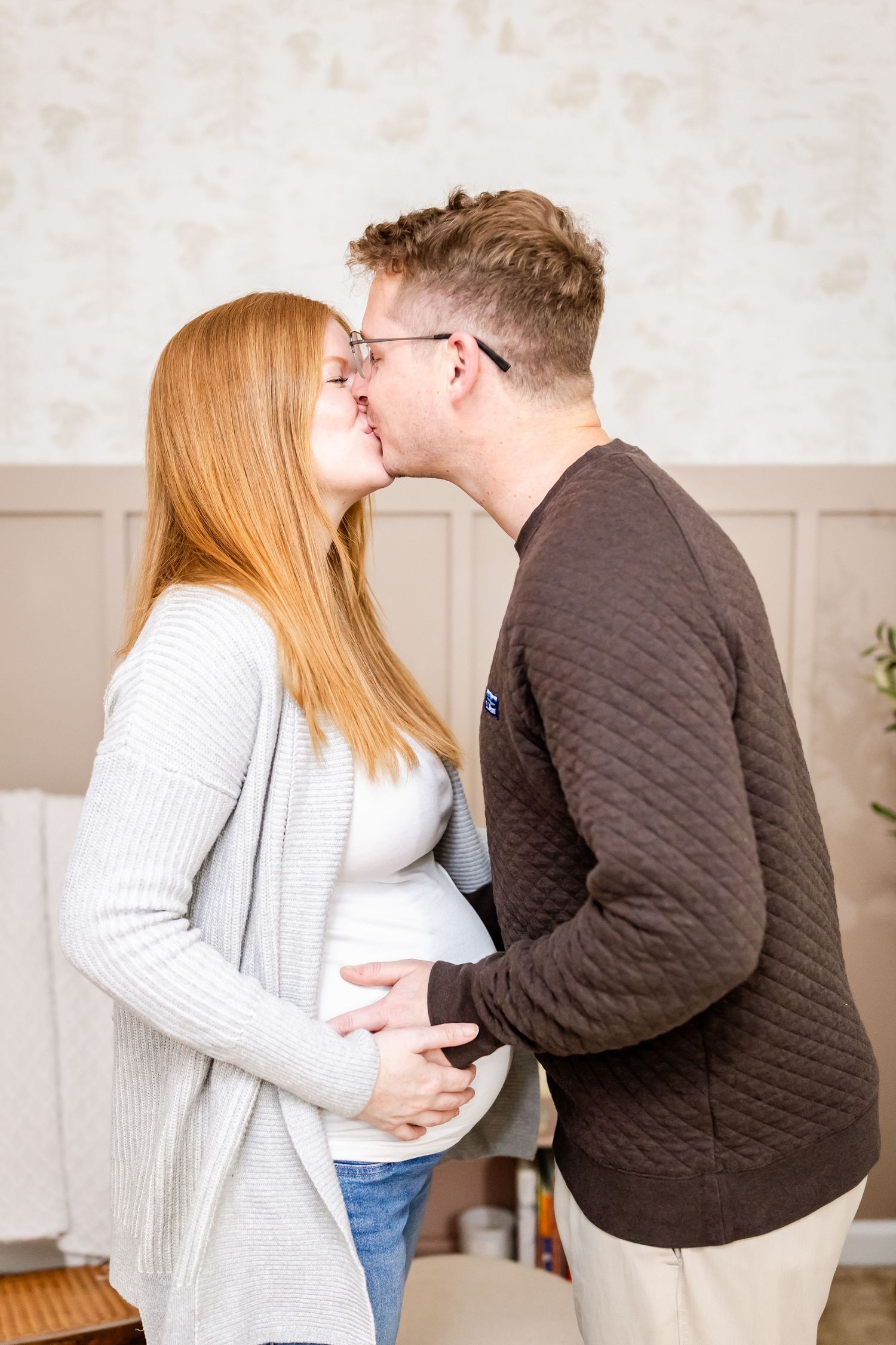 Expecting couple sharing an intimate moment with her showing a baby bump in a cozy indoor setting.