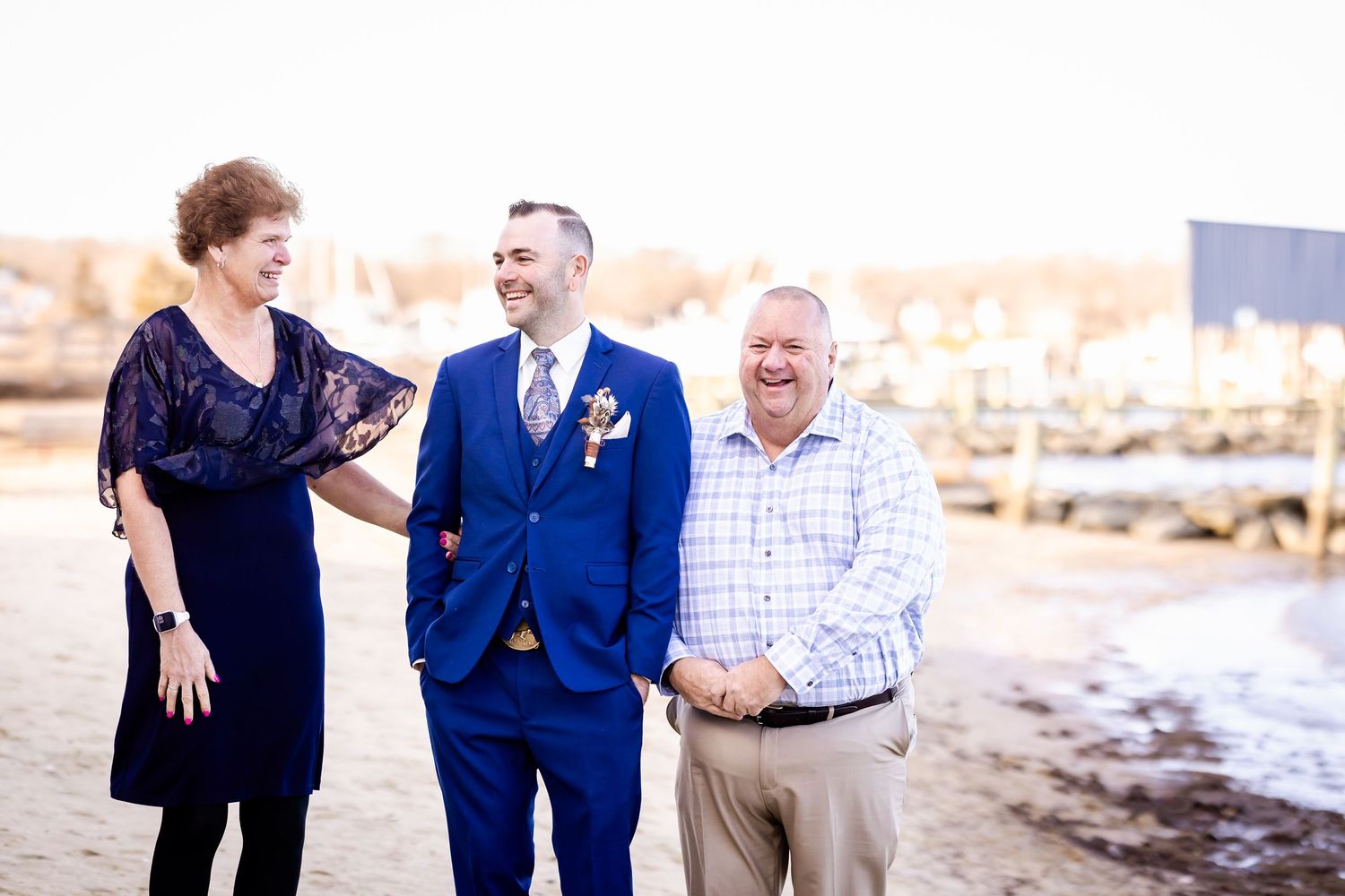 Three people sharing a joyful moment together on a beachfront, with one wearing a navy blue suit.