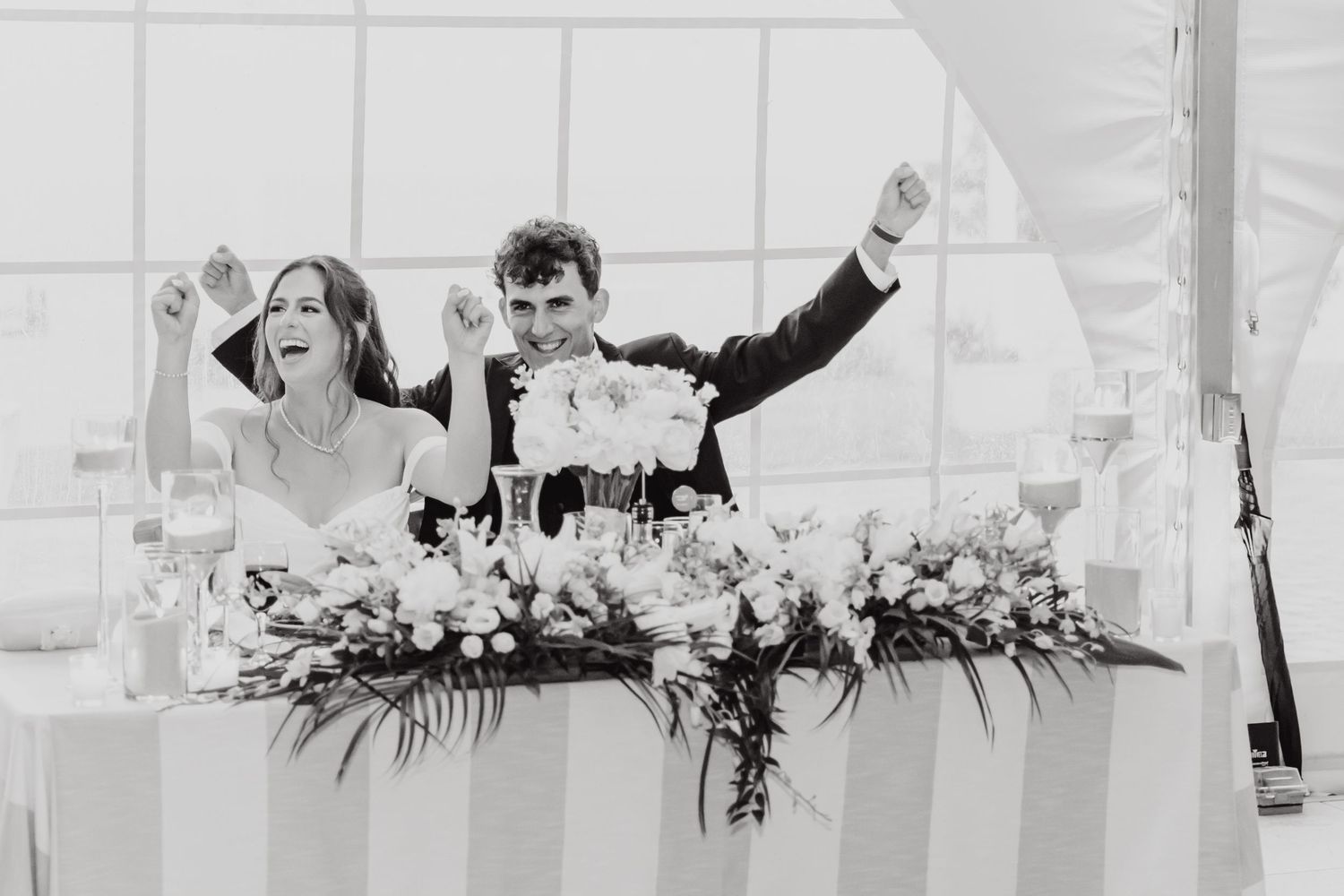 Black and white photo of a wedding reception head table with floral arrangements.