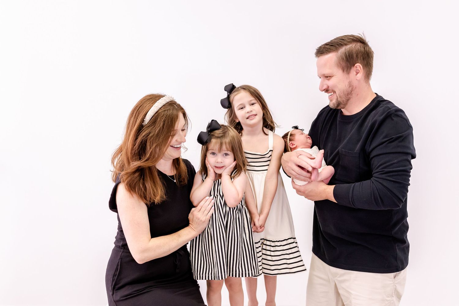 Family playfully interacts while sitting on light couch against a white backdrop in a photography studio.