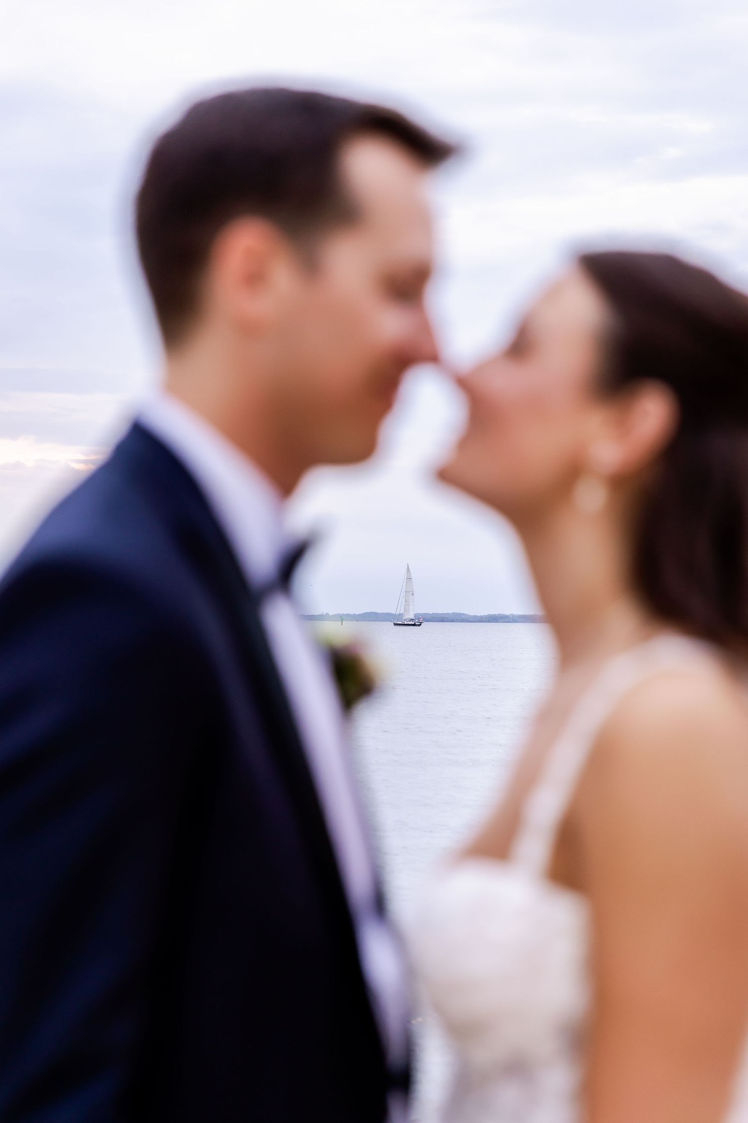 A soft focus romantic moment between newlyweds with a sailboat visible in the background.