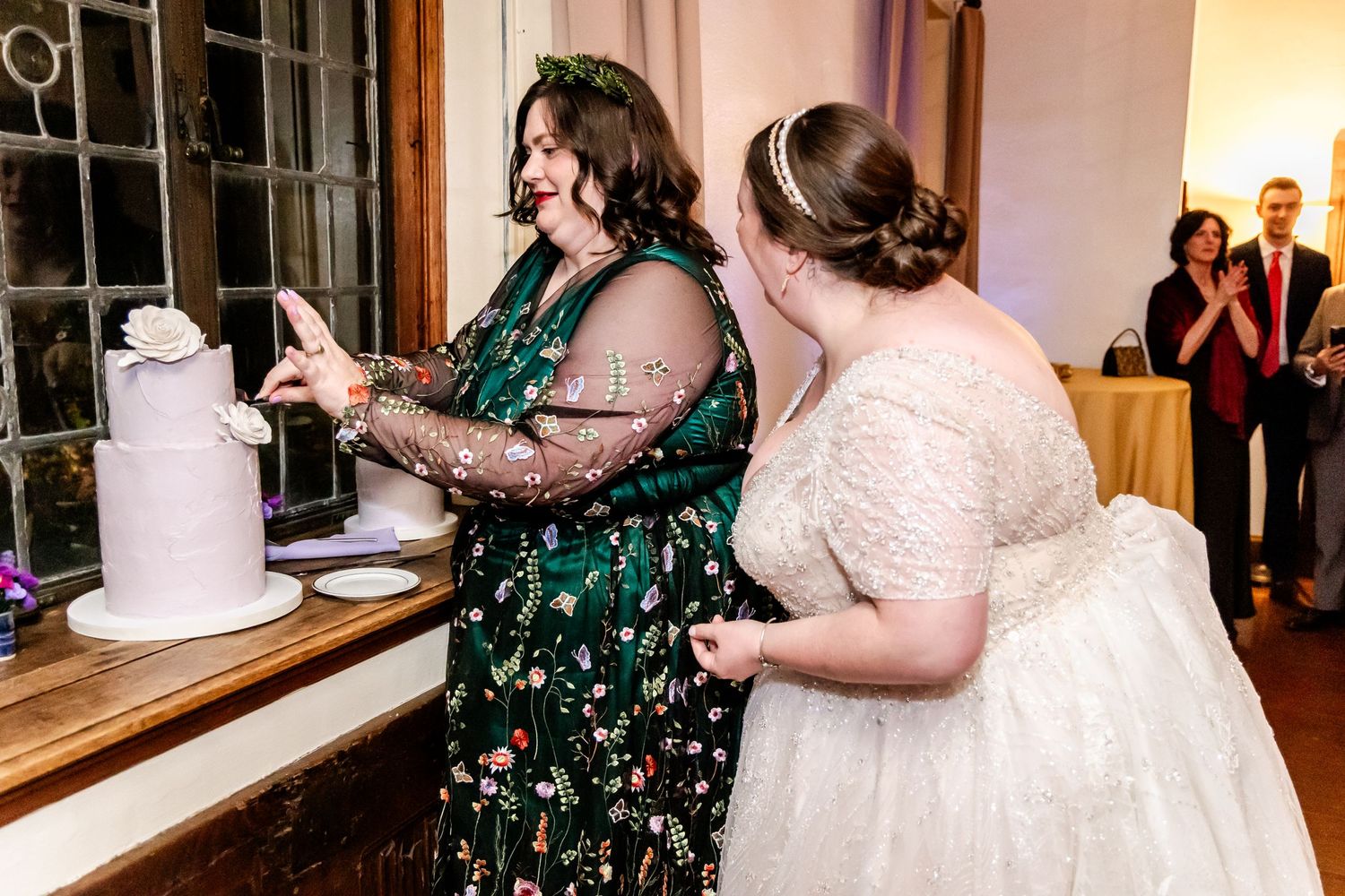 Two people cutting a white wedding cake together at a reception.