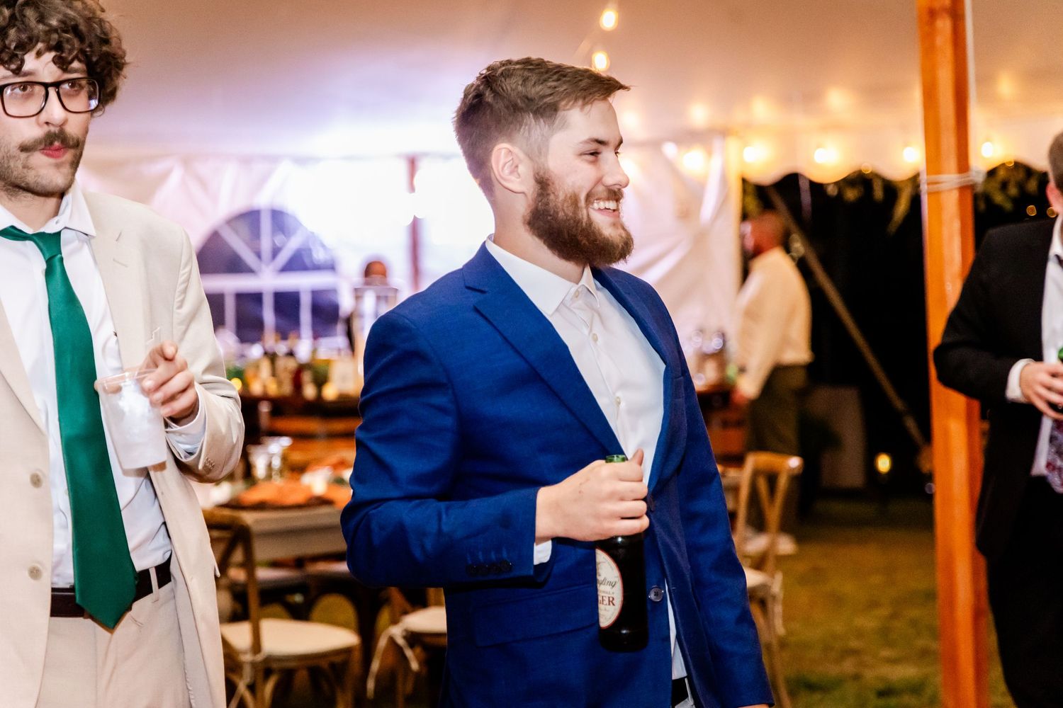 Wedding guests mingling and celebrating at reception under warm lighting.