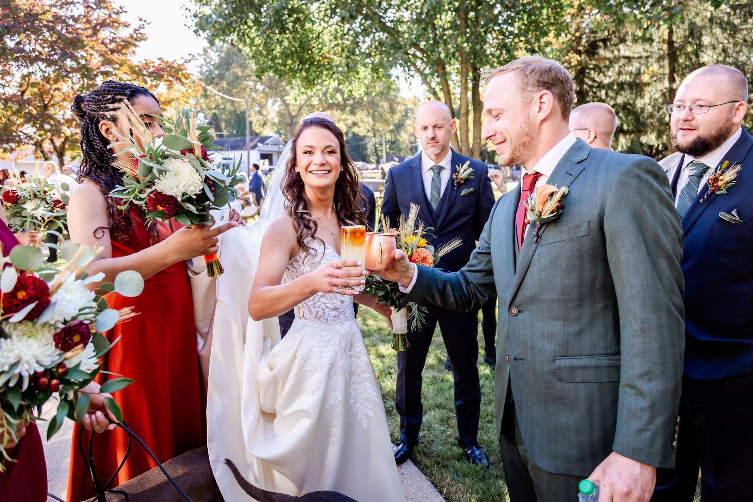 Wedding party members share drinks and laughter during an outdoor celebration.