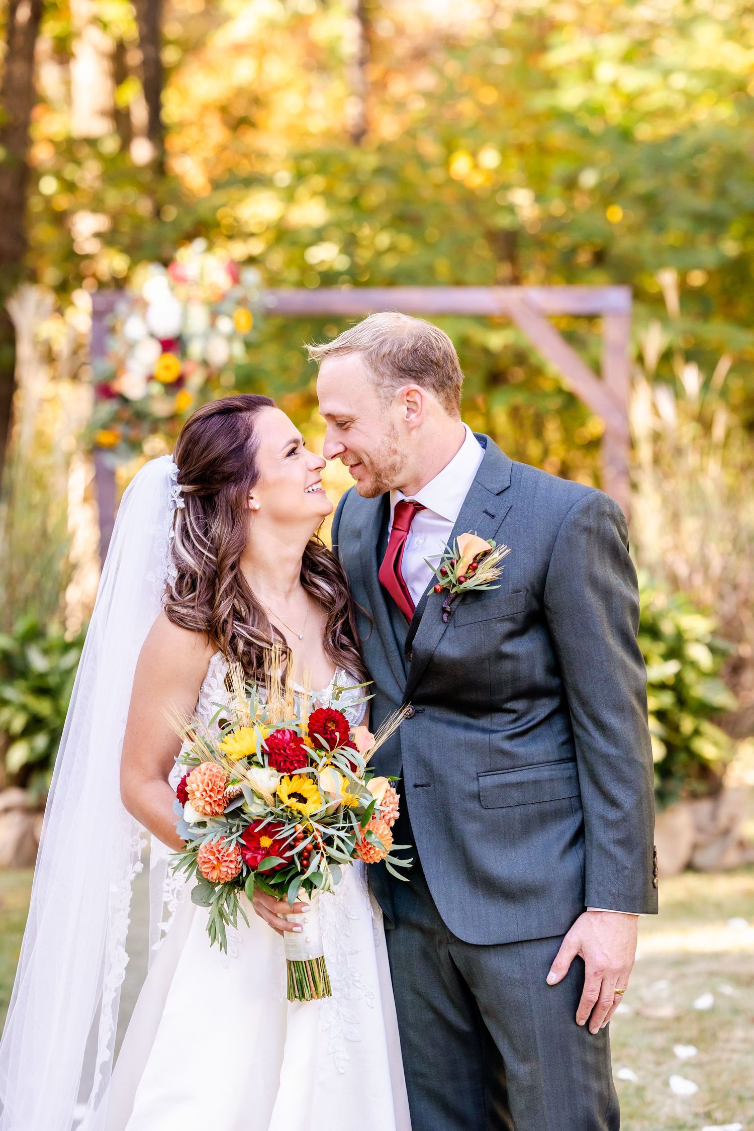 Newlyweds share romantic kisses in a garden setting with autumn colors and vibrant floral bouquet.