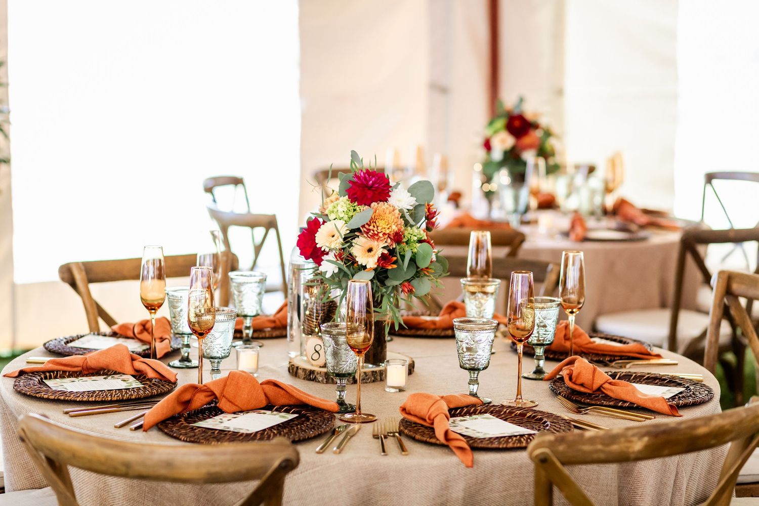 Elegant fall wedding table settings with orange accents and greenery runners on wooden tables.