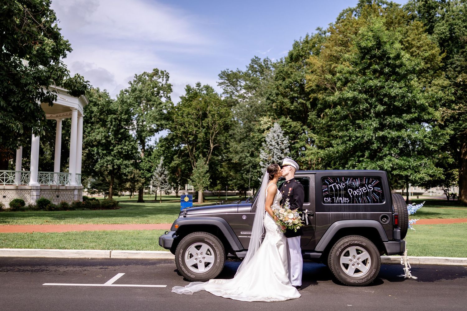 Wedding party poses with vintage Jeep outdoors on a sunny day.