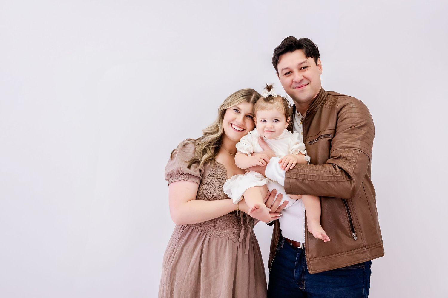 A family in neutral tones poses together for a series of studio portraits.