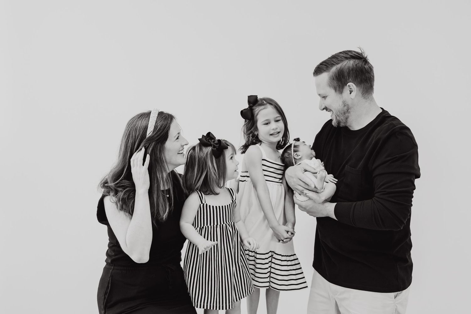 A joyful black and white photo of a family laughing together against a plain background.