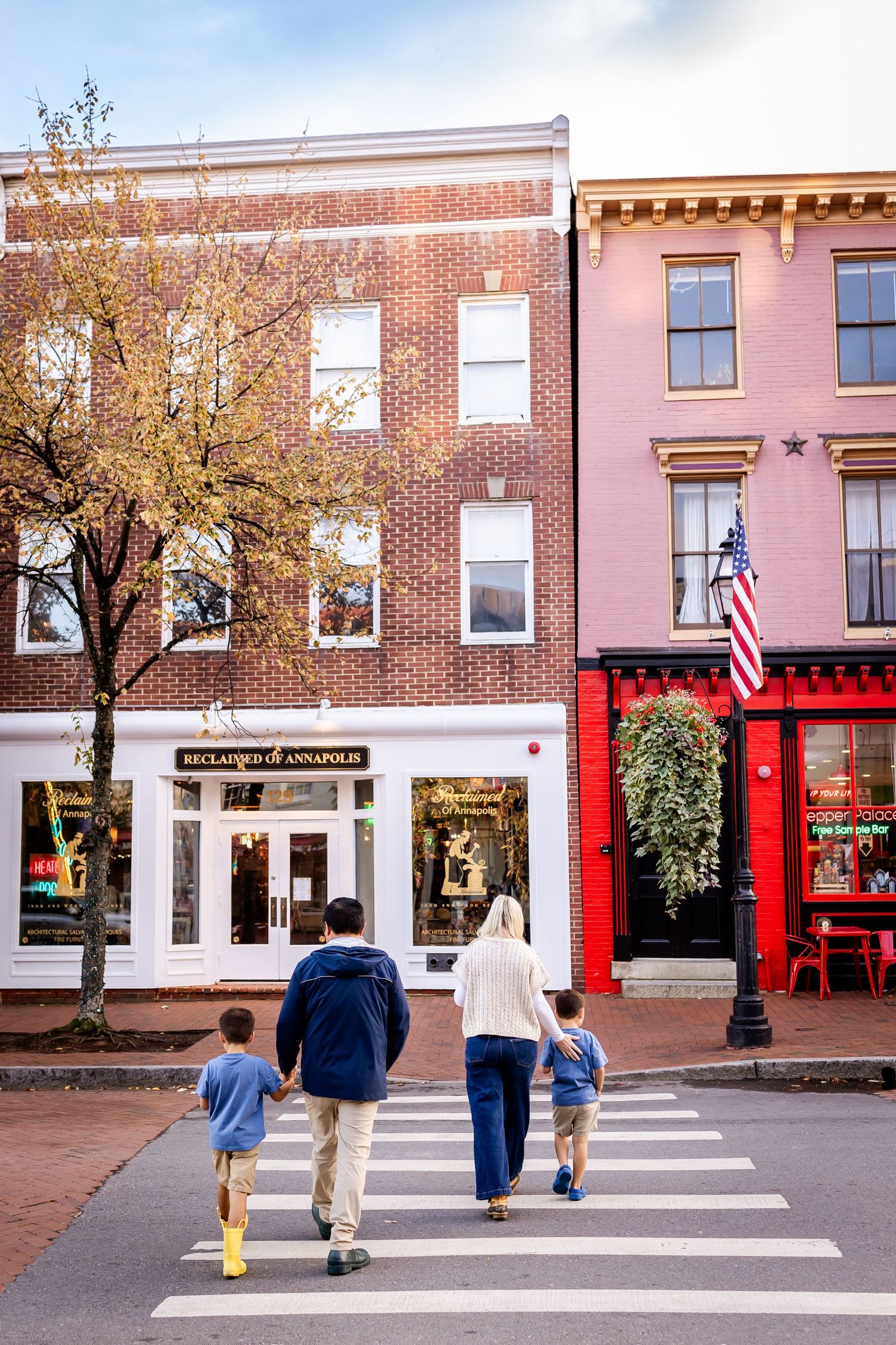 People walking across a crosswalk in front of historic brick buildings with American flags in a charming downtown area.