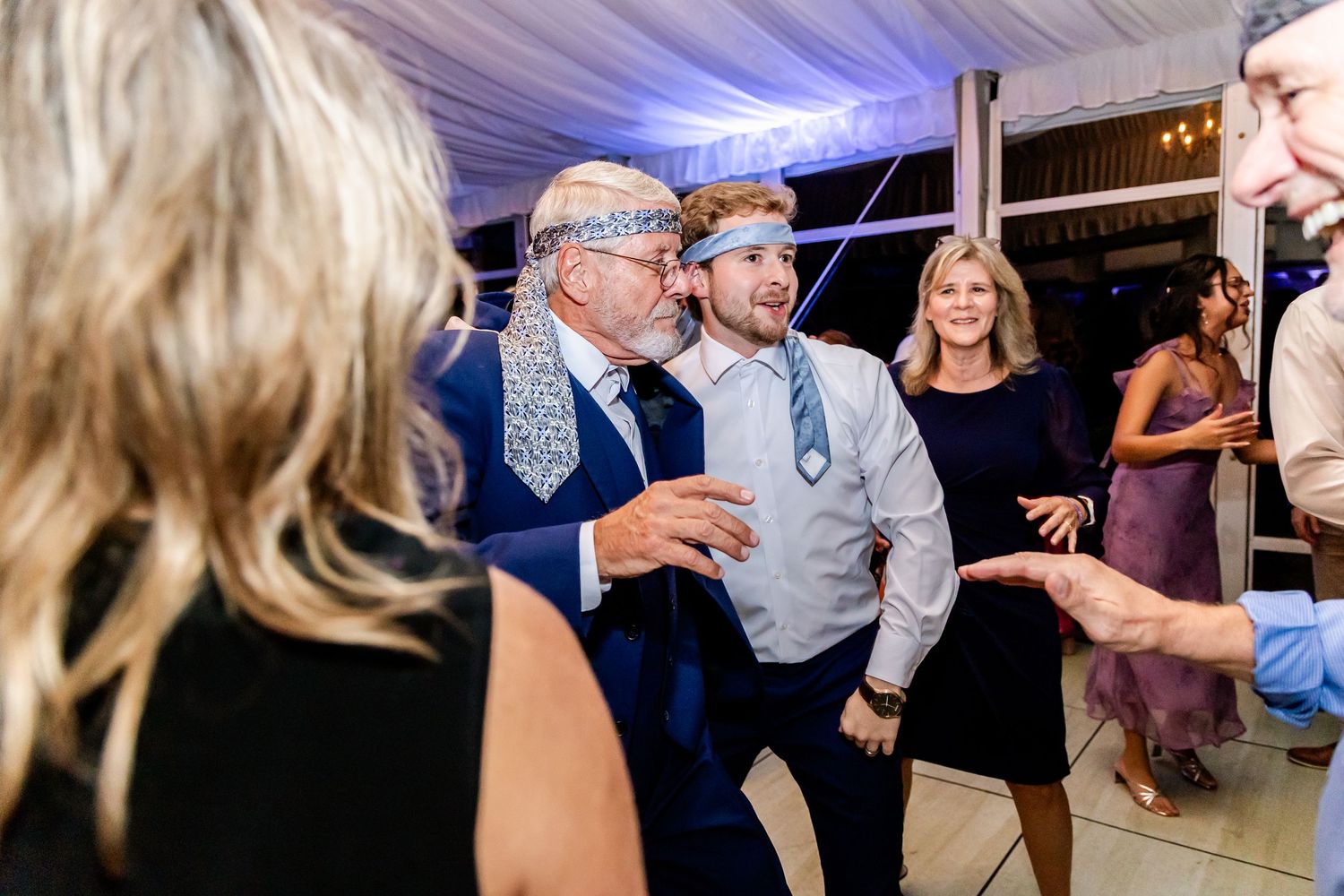 Guests dancing and celebrating at an evening wedding reception under blue-tinted lighting.