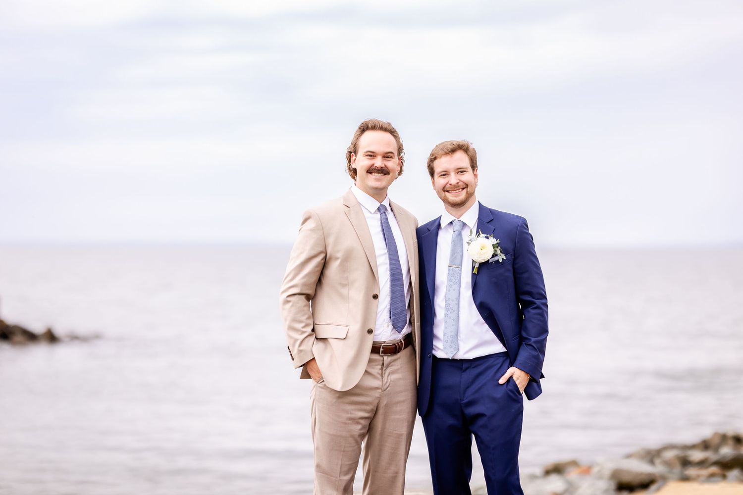 Guests celebrate and smile together during an outdoor beach wedding ceremony on an overcast day.