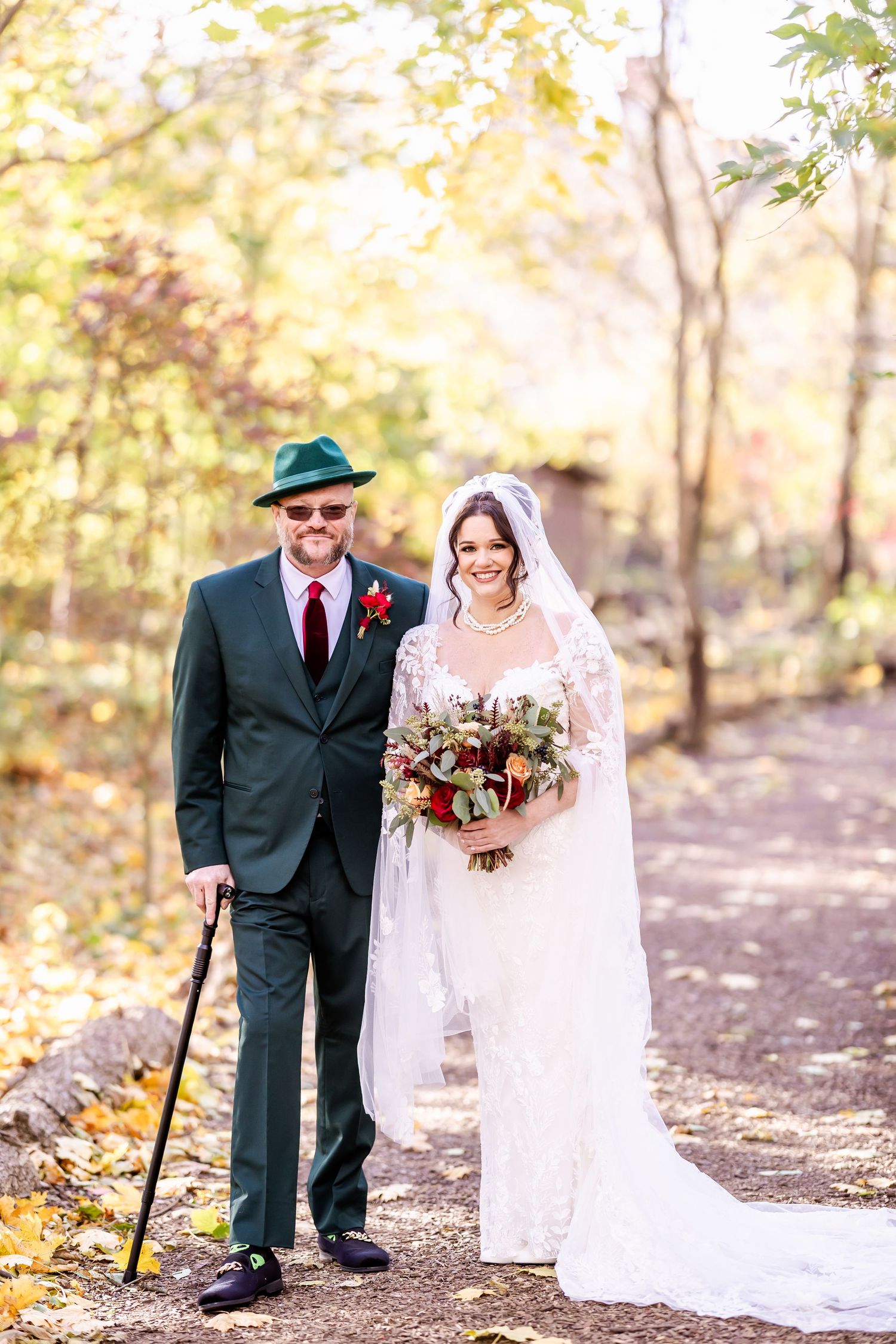 Wedding couple walking together through autumn woods with sunlit golden leaves in background.