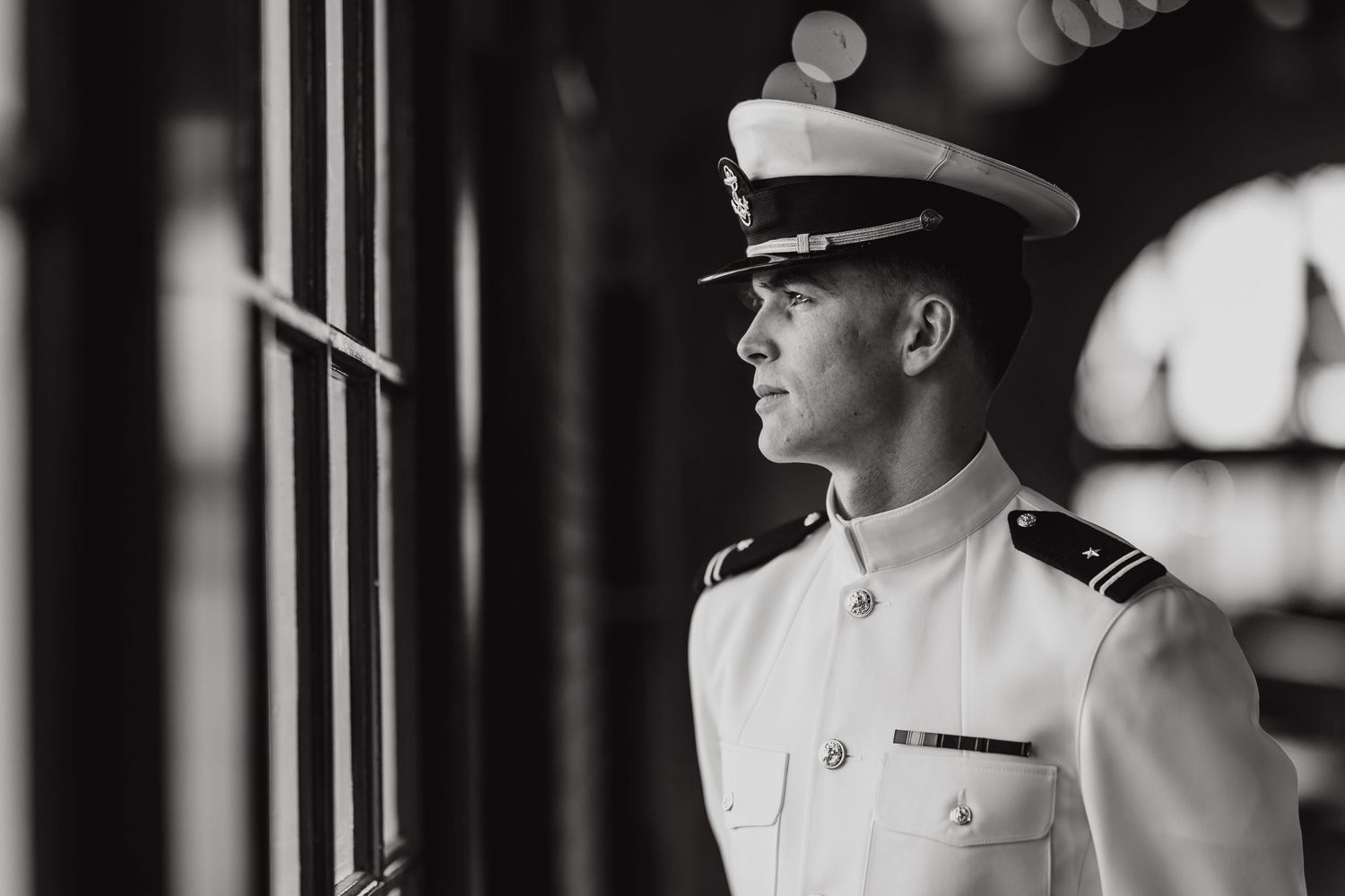 Black and white portrait of a young military officer in dress whites and cap gazing thoughtfully to the side.