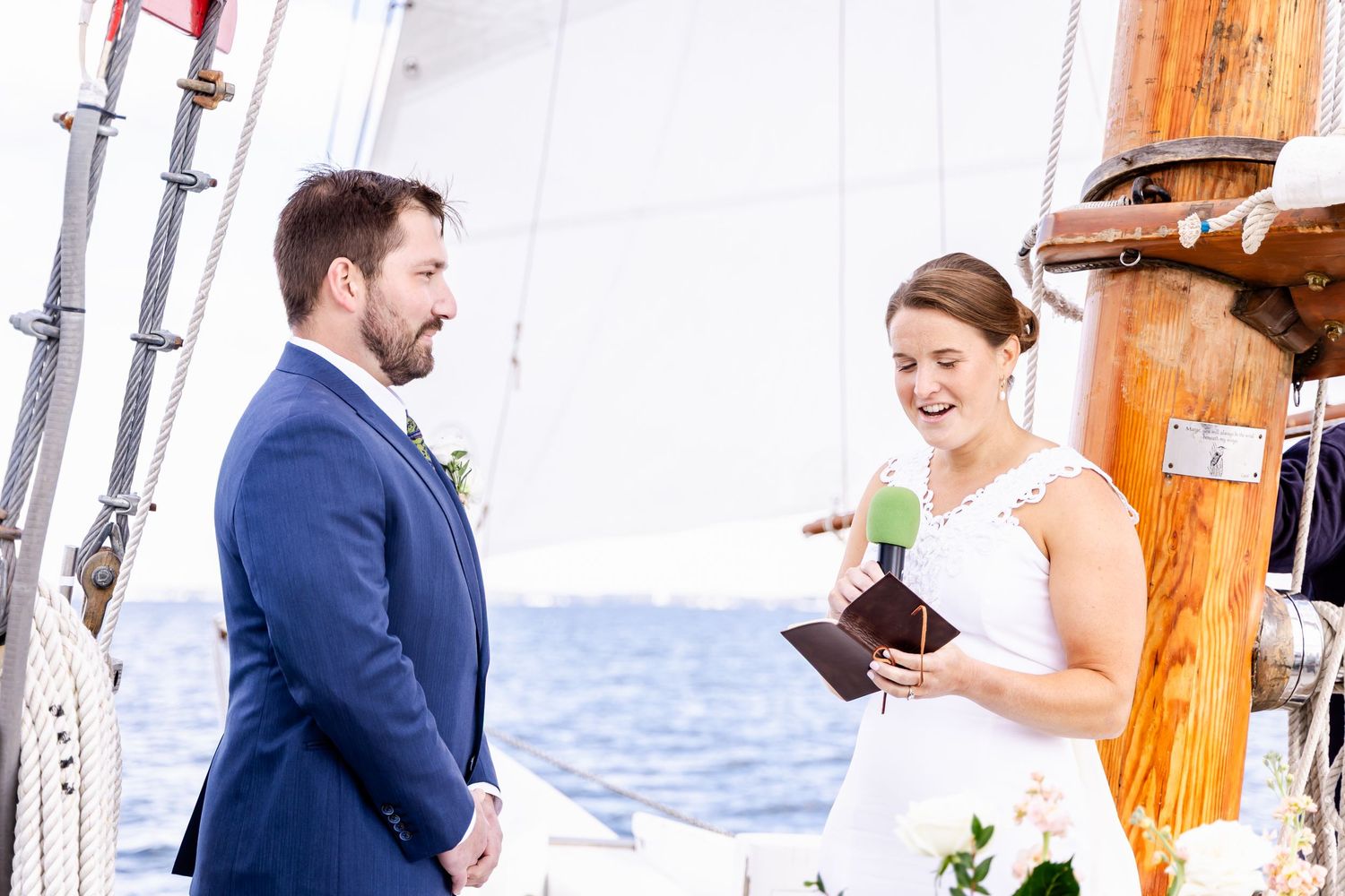 Bride laughing while reading vows to groom during romantic outdoor sailing wedding ceremony on the ocean.