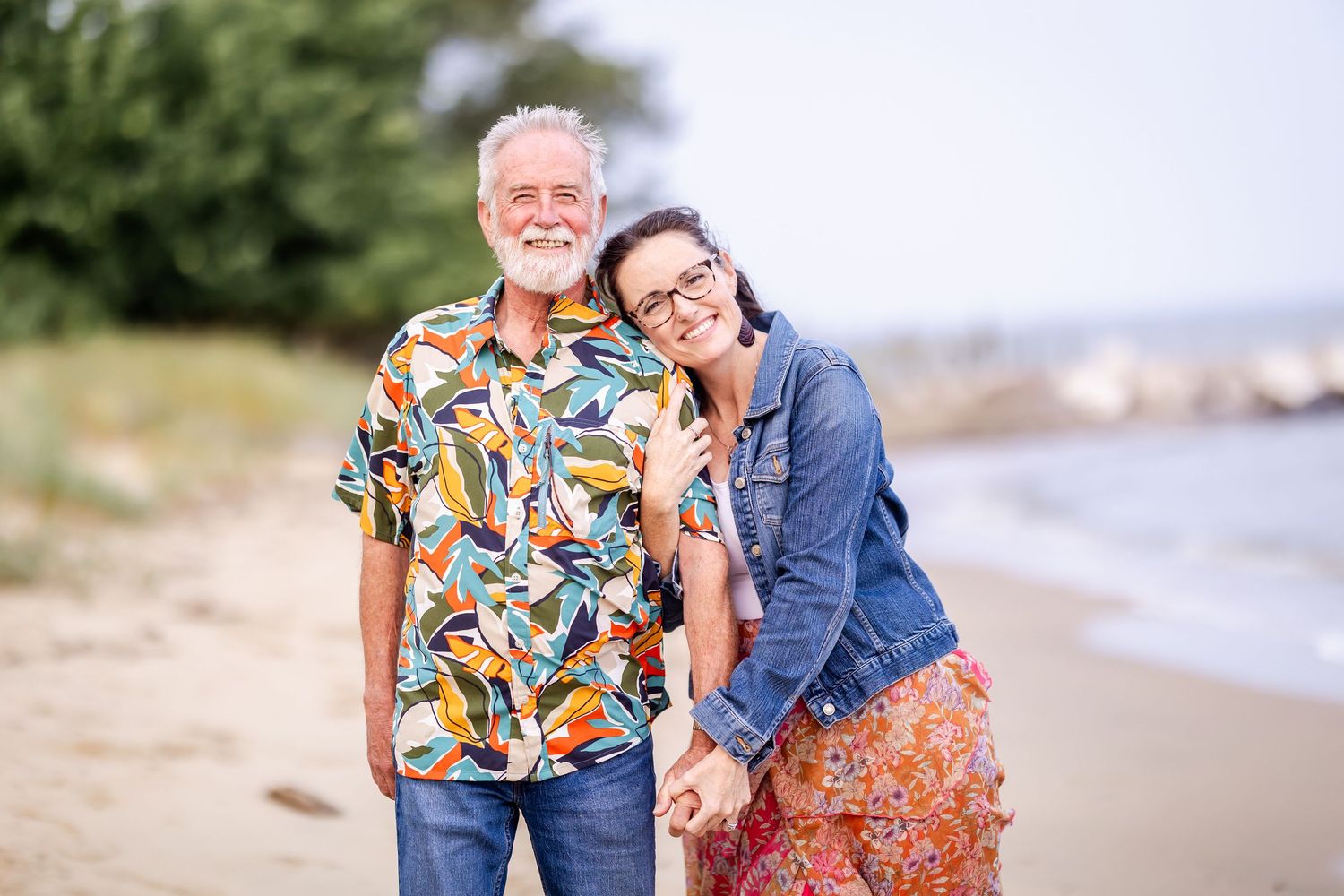 A couple walks along a scenic beach wearing colorful tropical shirts and floral dresses on a sunny day.