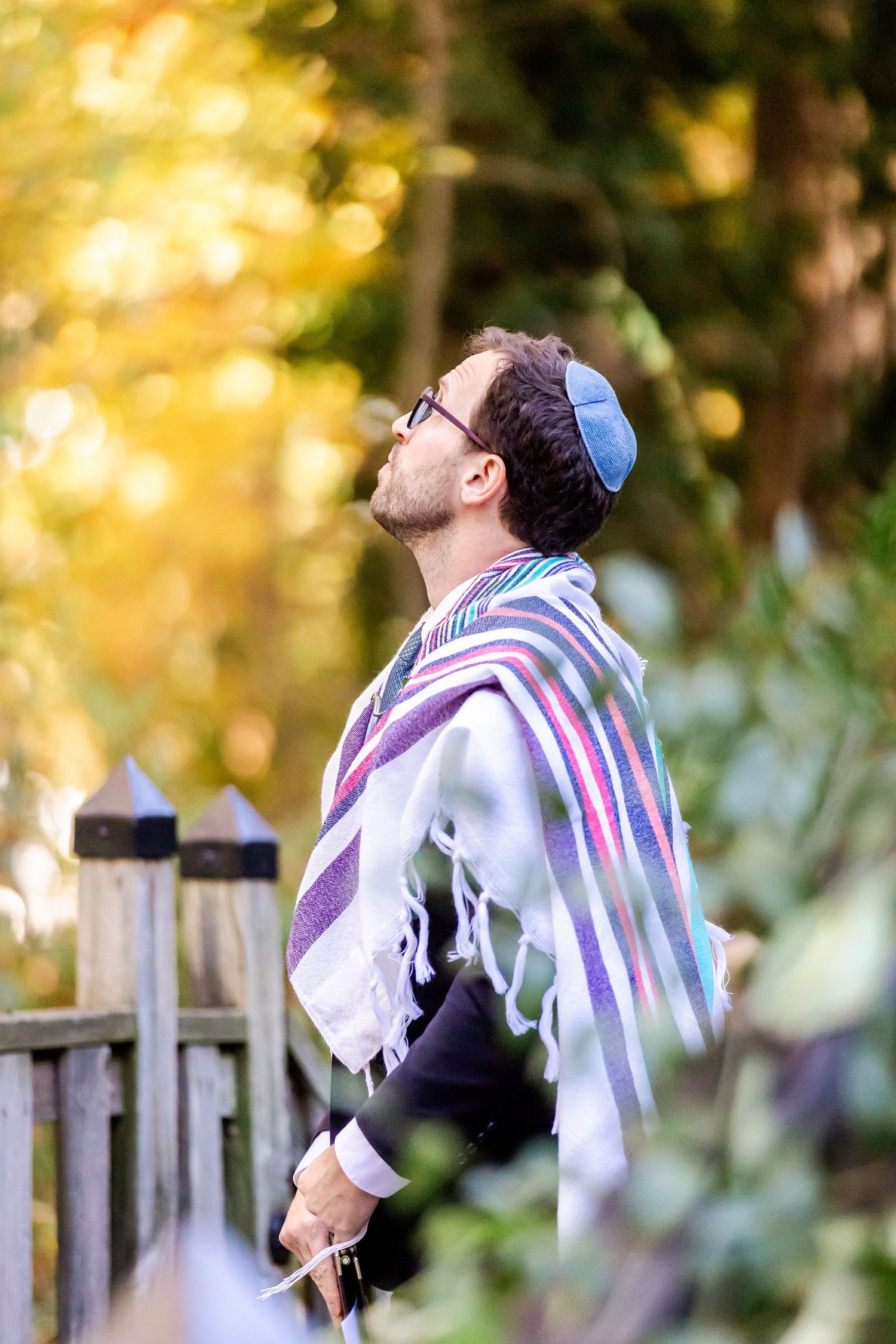 Person in prayer shawl and kippah looking upward during an outdoor Jewish ceremony.