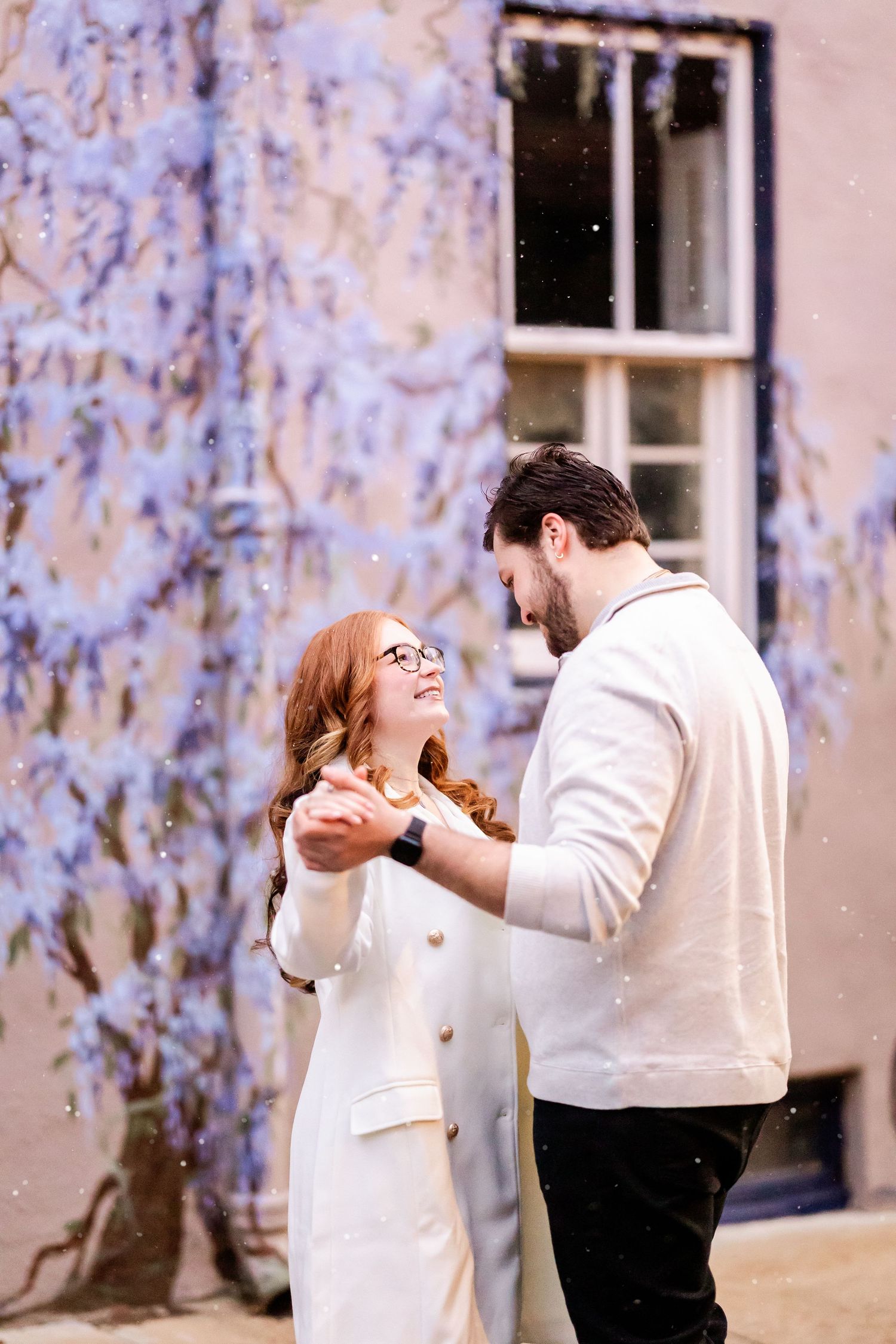A couple in white attire share a romantic dance sequence outdoors against a light blue floral backdrop.