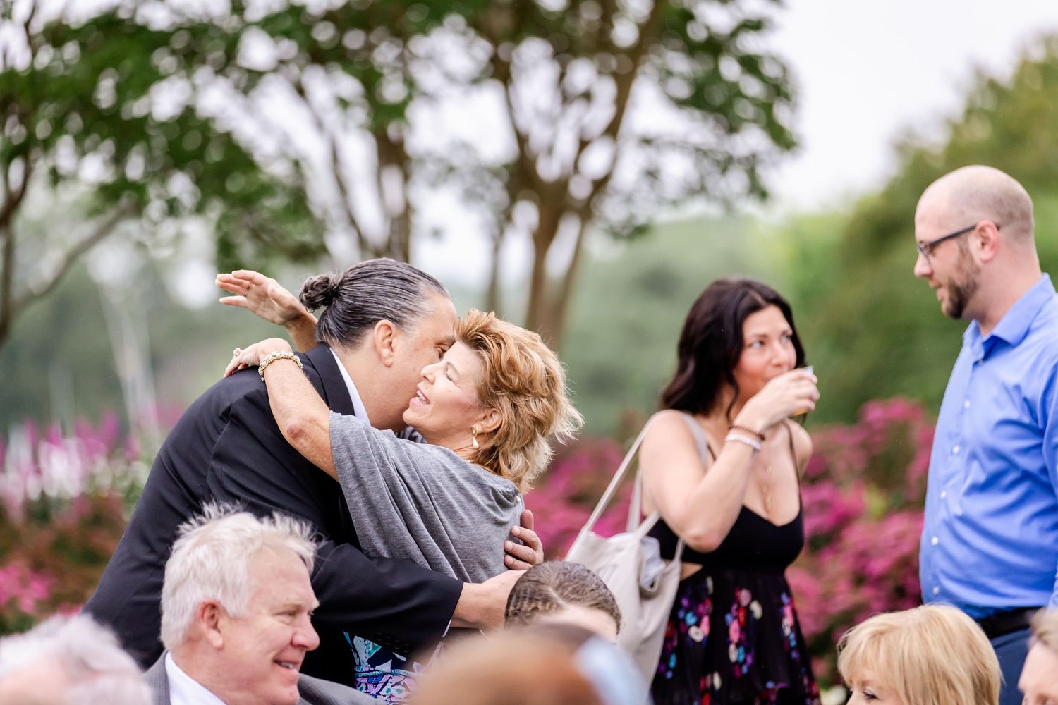 Wedding guests dance and celebrate at an outdoor reception with trees in the background.
