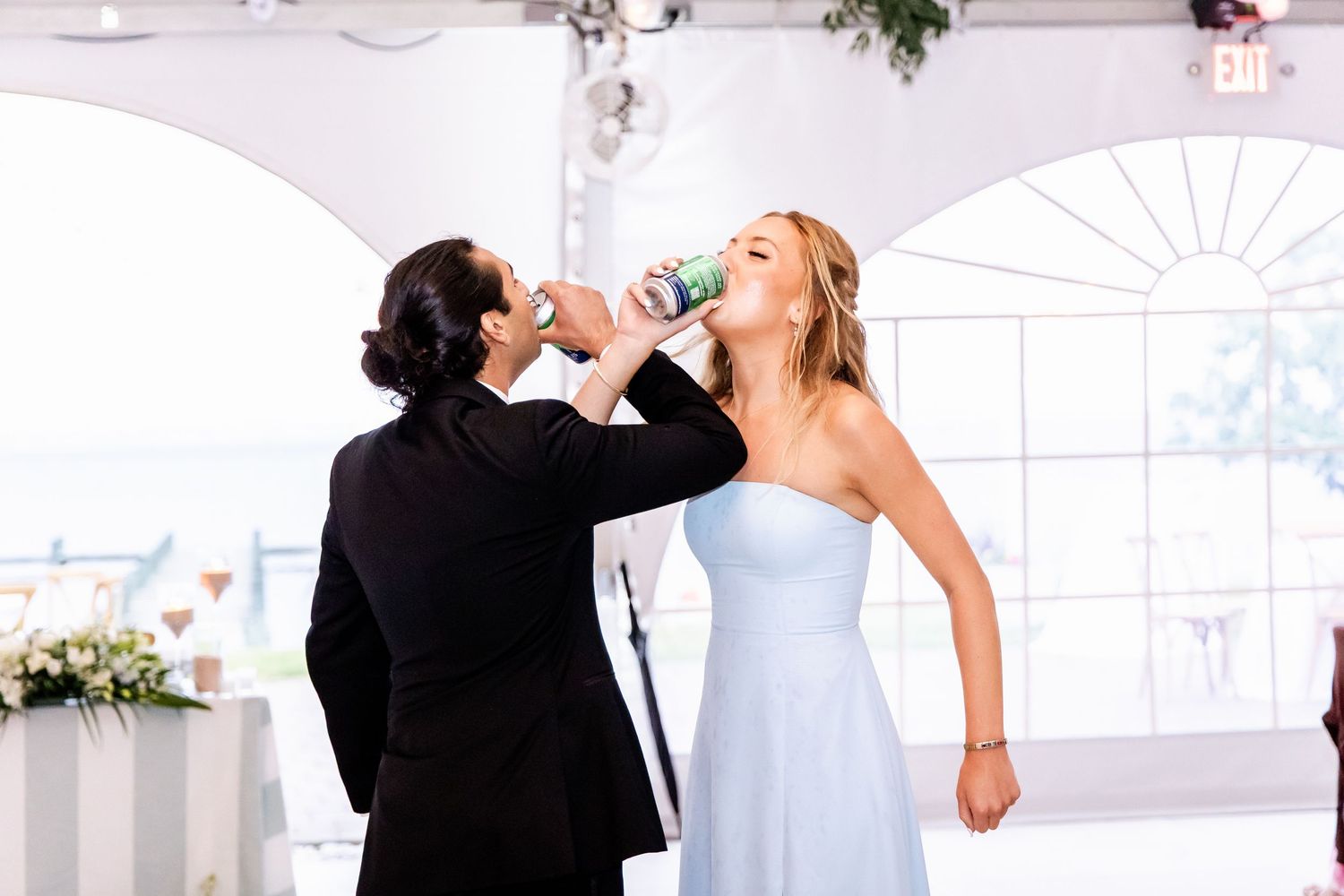 Two people in formal attire sharing a celebratory drink at an elegant white-themed venue.