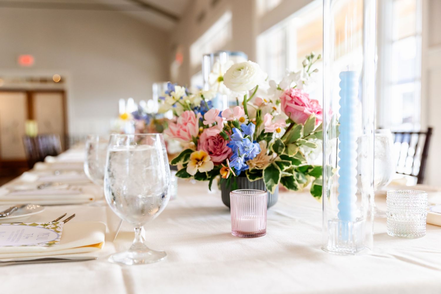 An elegant wedding table centerpiece with pink and blue flowers in a glass vase.