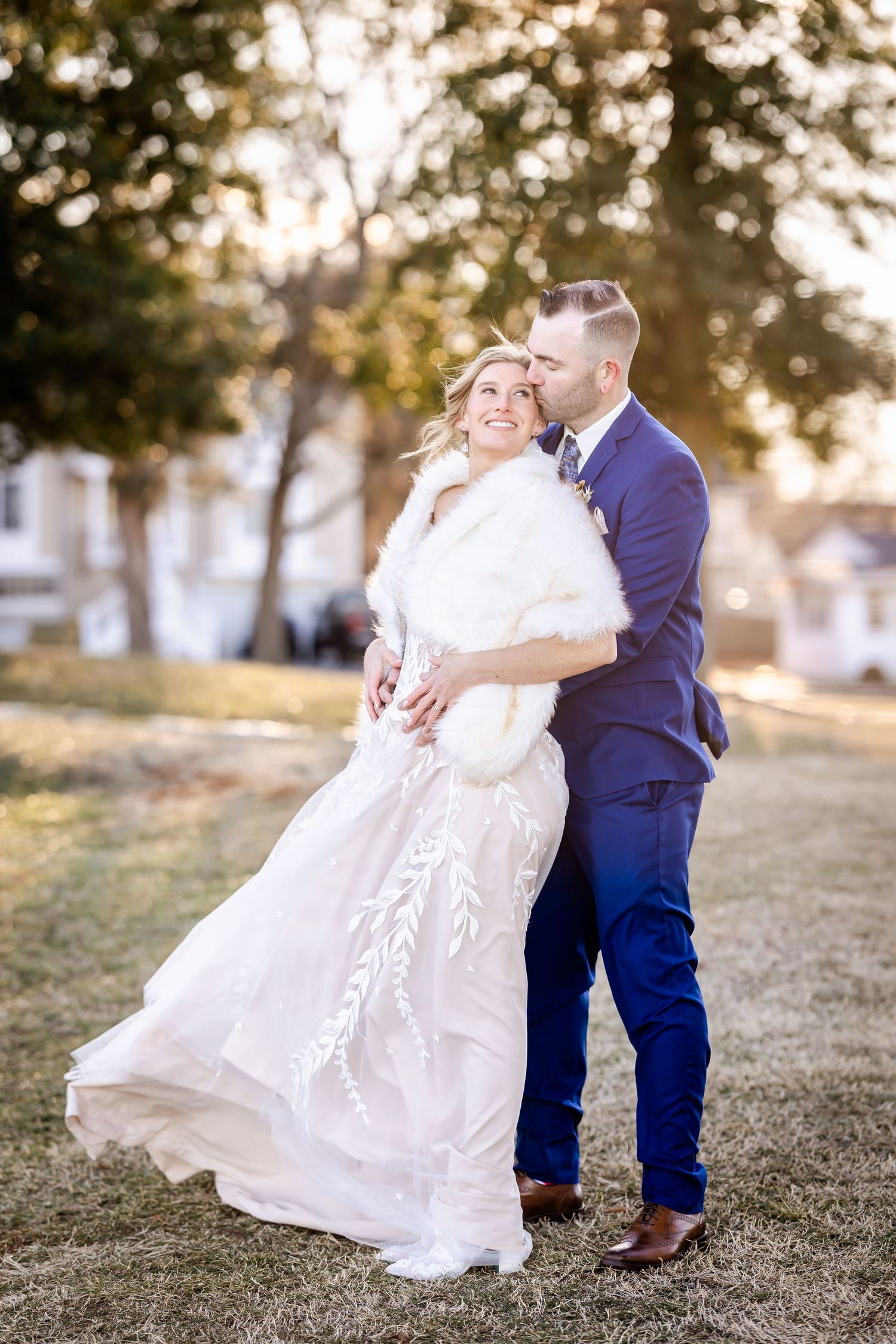 Joyful wedding couple shares intimate moment outdoors in blue suit and lace gown with fur shawl.