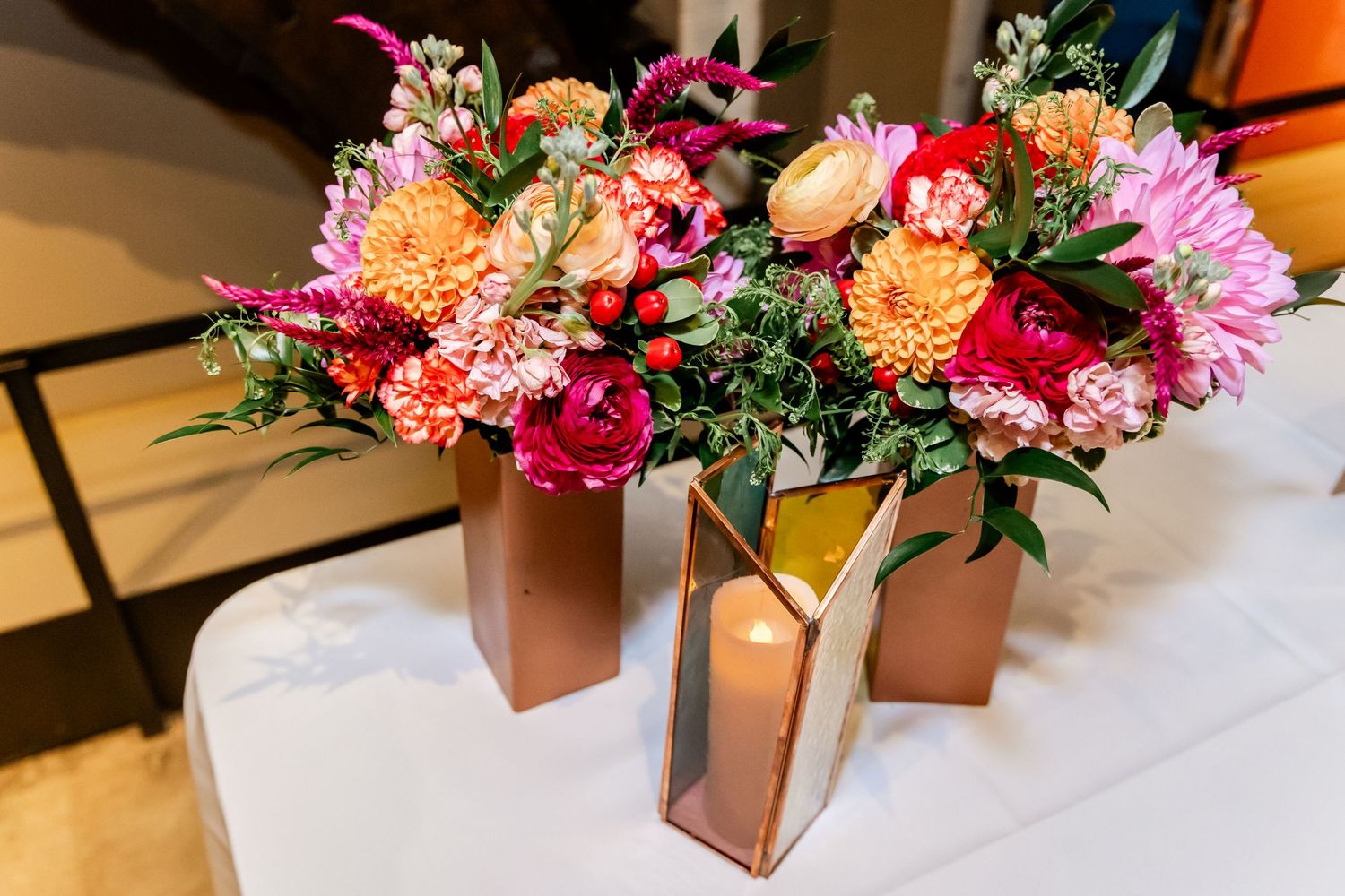 Vibrant floral arrangements with pink, orange and purple blooms in copper geometric vases.