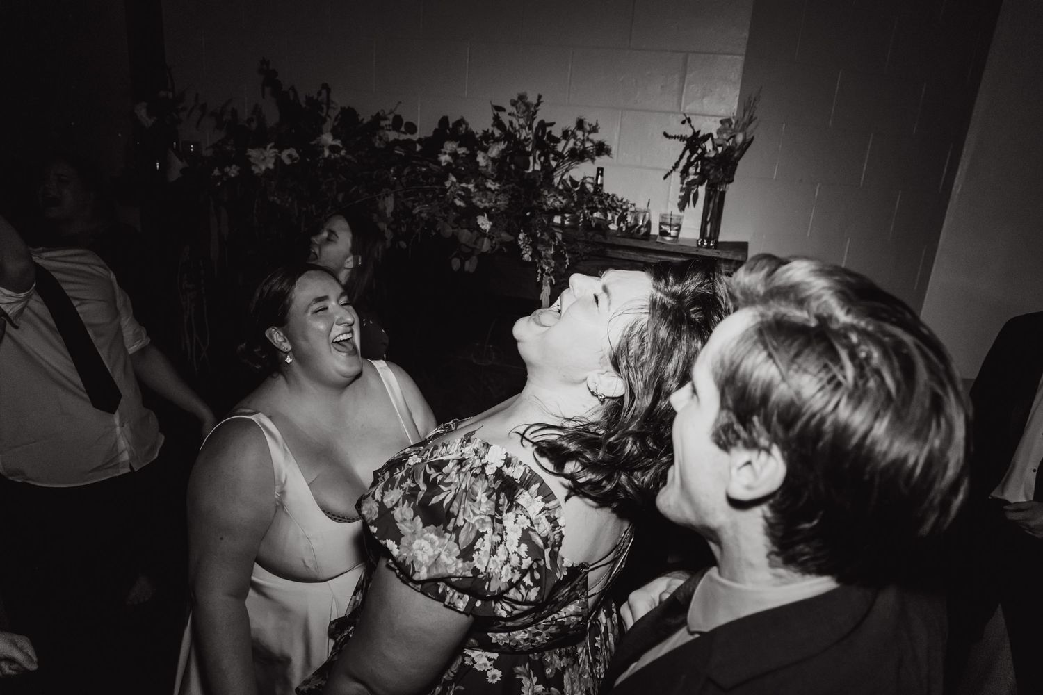 Black and white candid shot of wedding guests laughing and dancing at a reception.