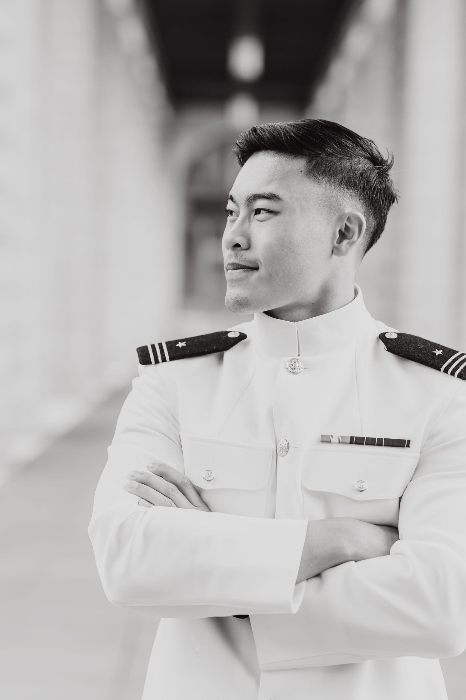 Naval officer in white dress uniform stands with arms crossed in black and white portrait photograph.