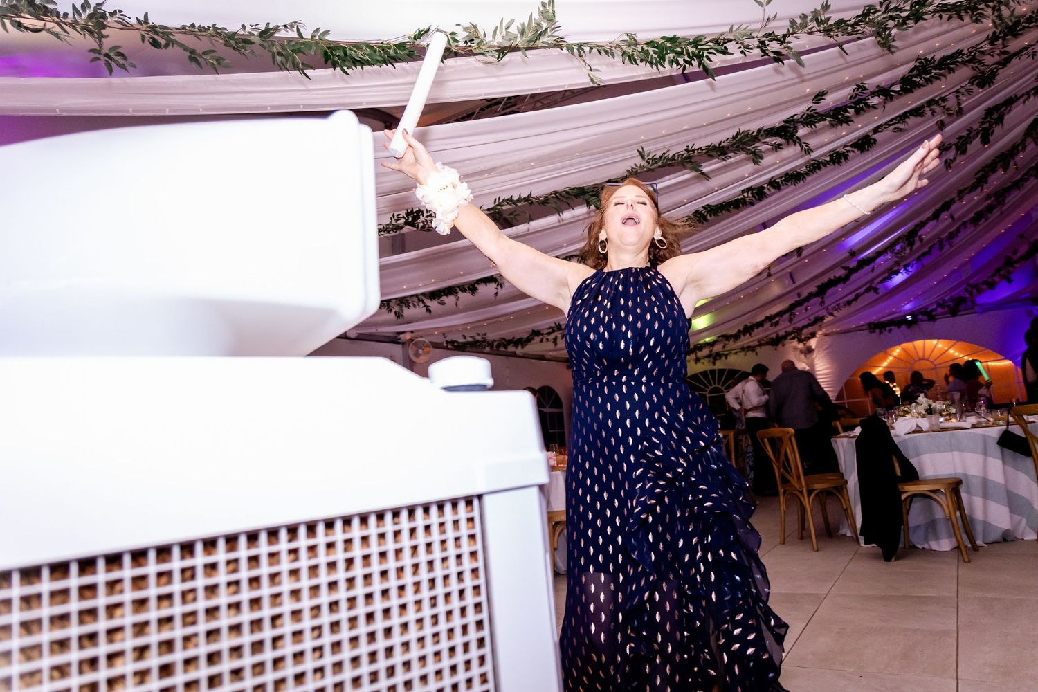 Wedding guest in polka dot dress dancing beneath draped fabric and purple lighting at reception.
