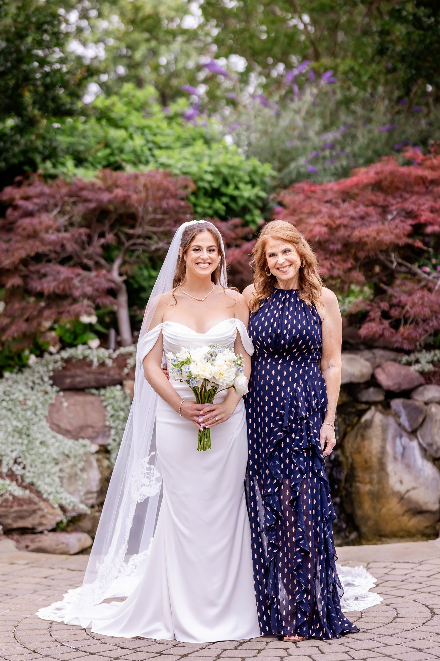 A wedding scene in a garden with Japanese maple trees and stone wall backdrop.