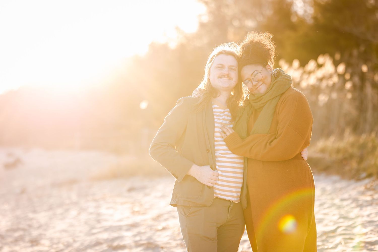 Two people in cozy winter wear share warm embrace in golden sunlight.