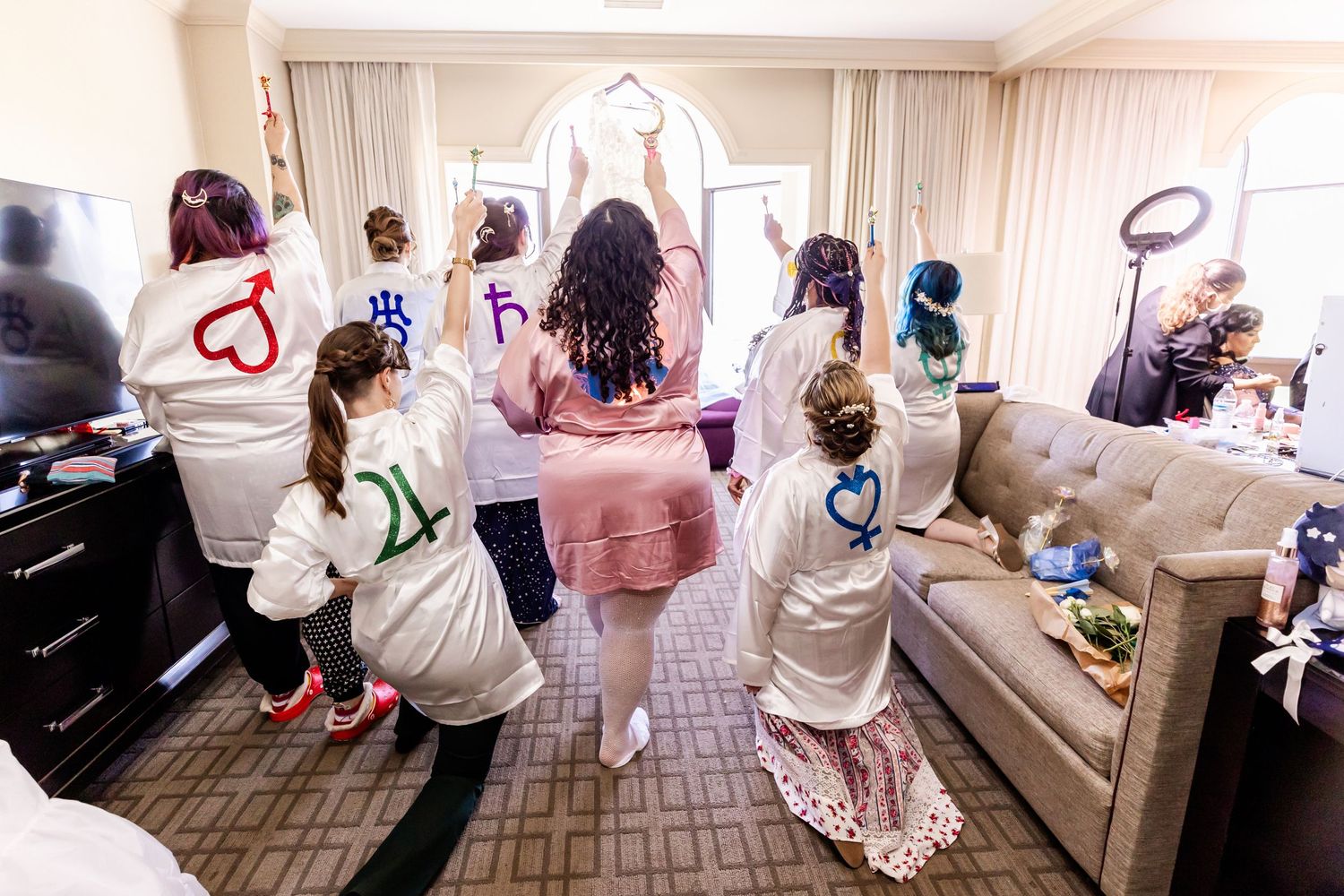 Group in matching robes celebrating in a hotel room during wedding preparations.