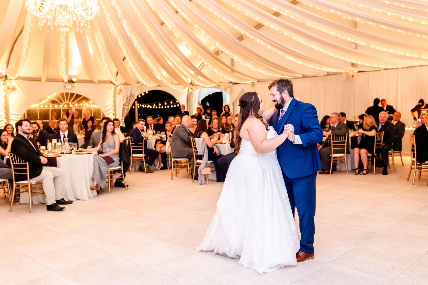 Wedding reception first dance in an elegant tent venue with ambient lighting and seated guests.