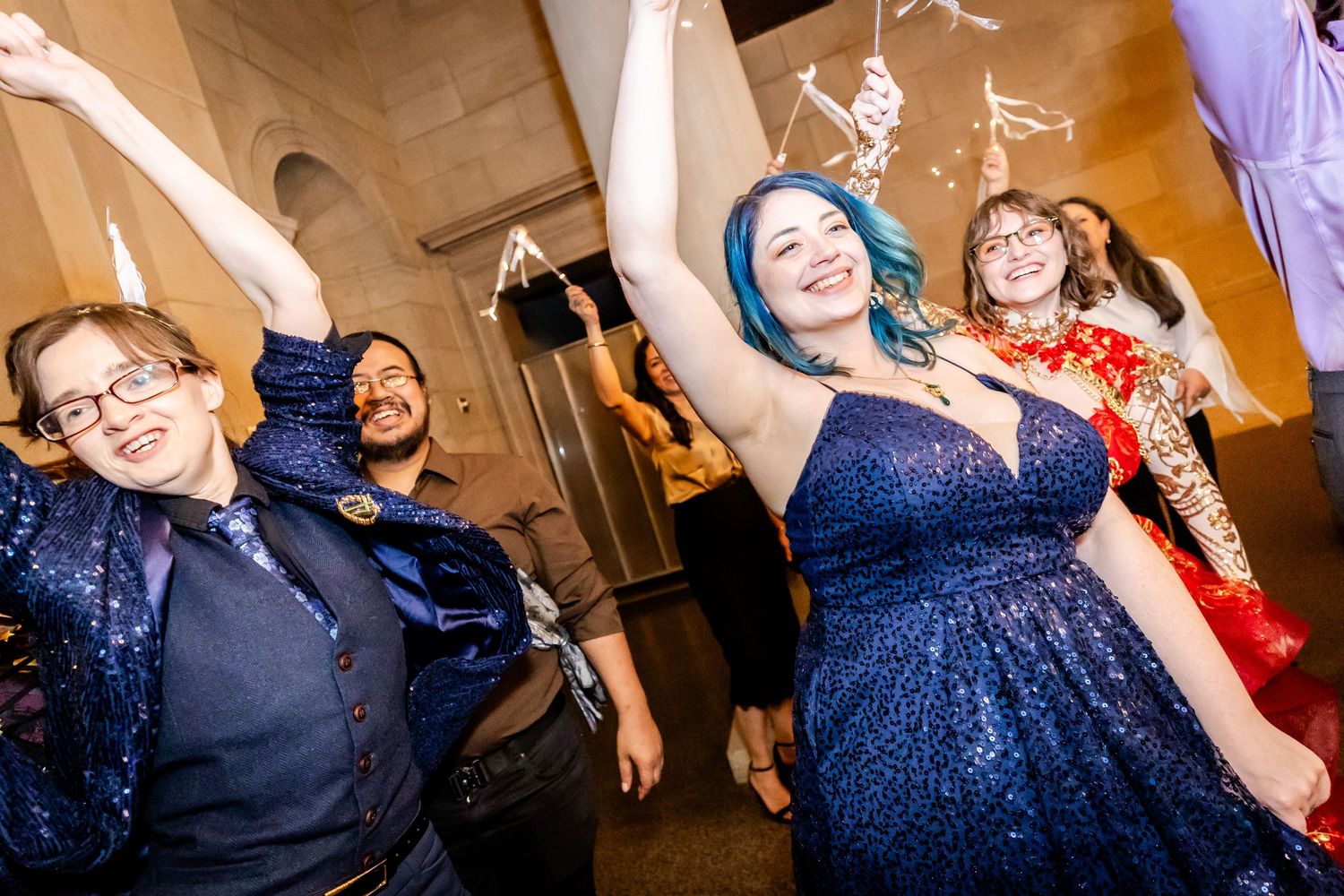 Wedding guests dancing and celebrating with raised arms in a beautifully lit venue.
