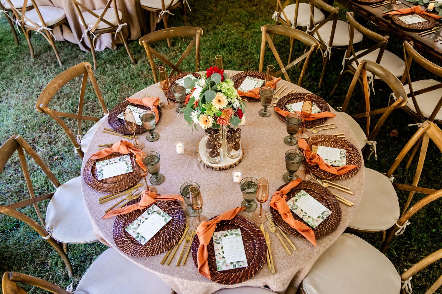 Elegant round table setting with rustic decor and cross-back chairs at a wedding reception.