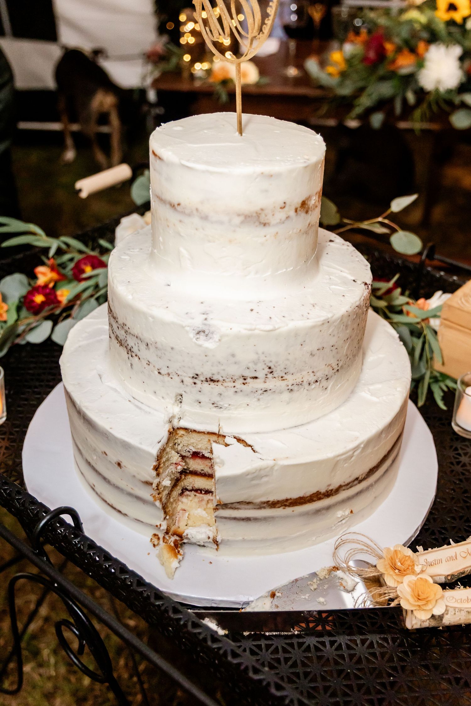 White tiered wedding cake with rustic frosting displayed on black stand with floral decorations.